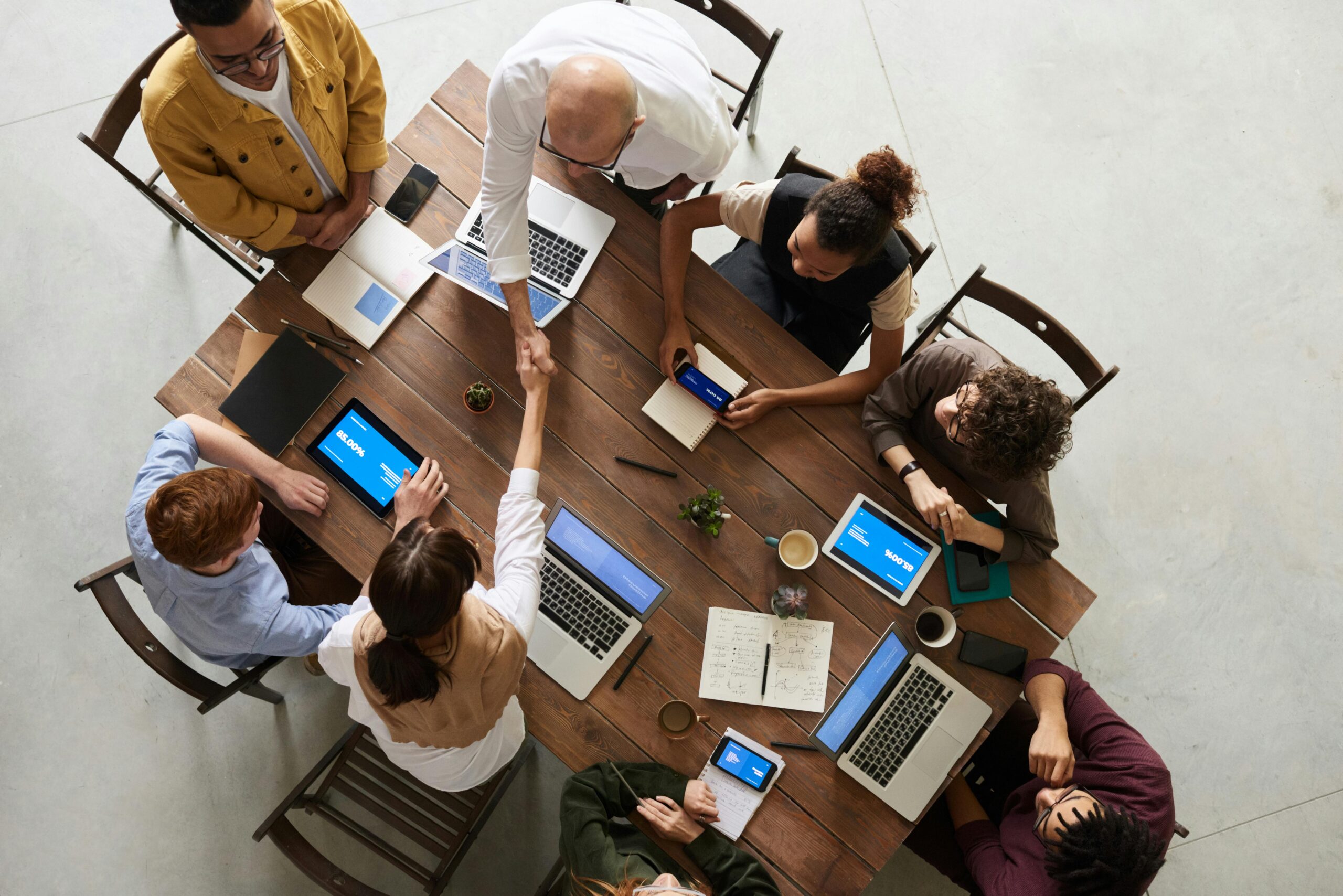 About Top view of a diverse team collaborating in an office setting with laptops and tablets, promoting cooperation.