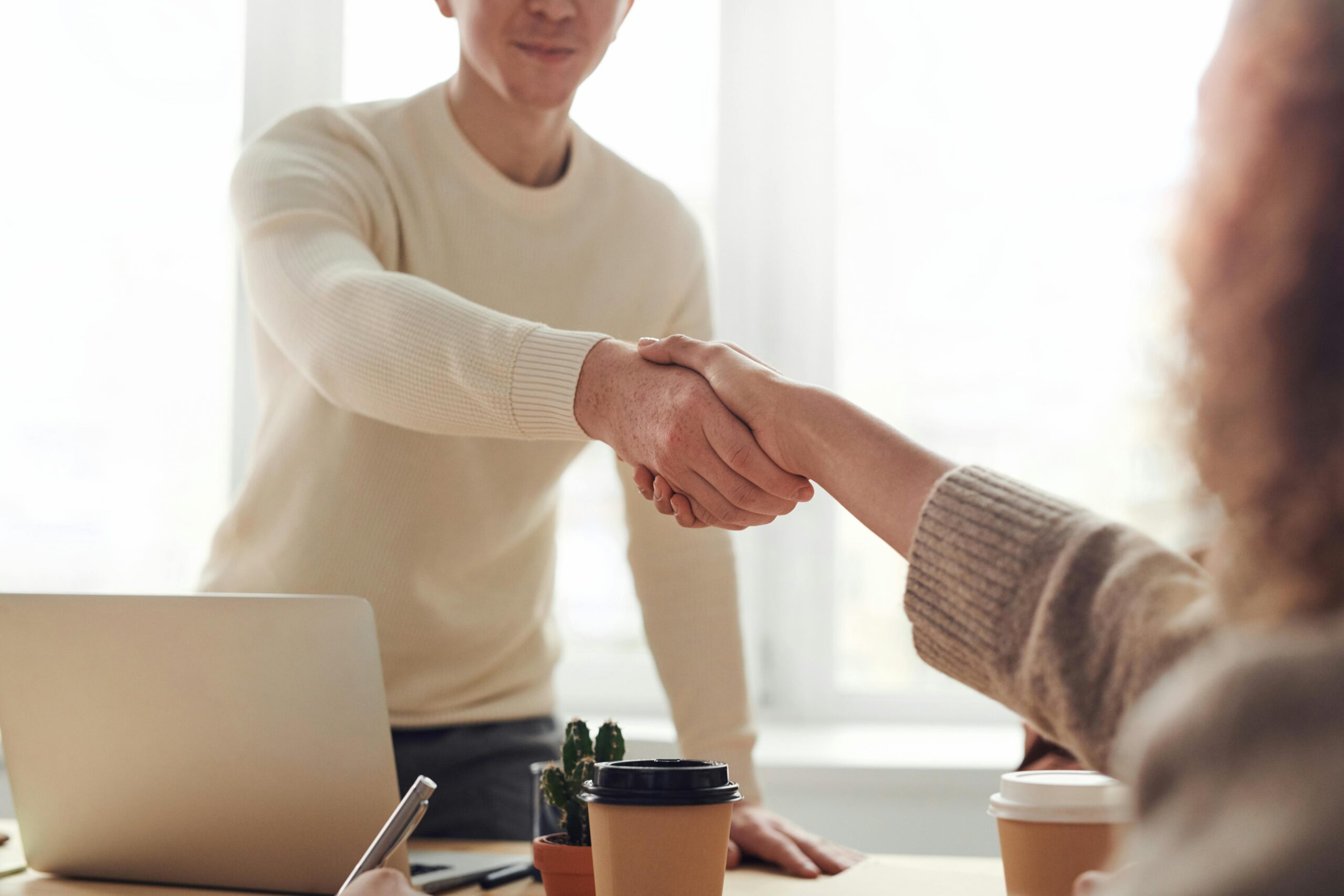 Contact Close-up of professionals shaking hands over coffee in a modern office.