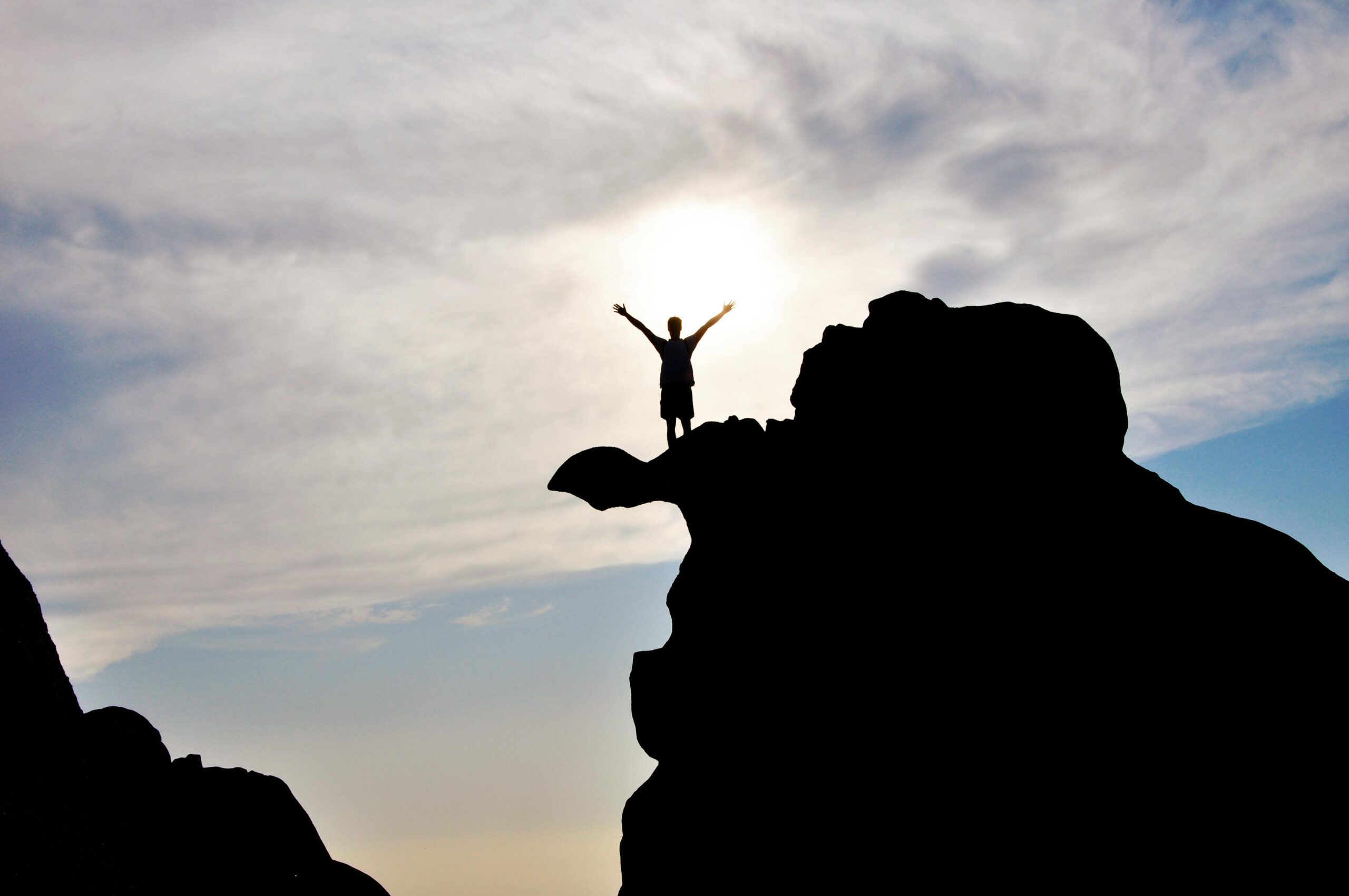 Services Silhouette of a person celebrating on a mountain peak against a dramatic sky, symbolizing freedom and success.