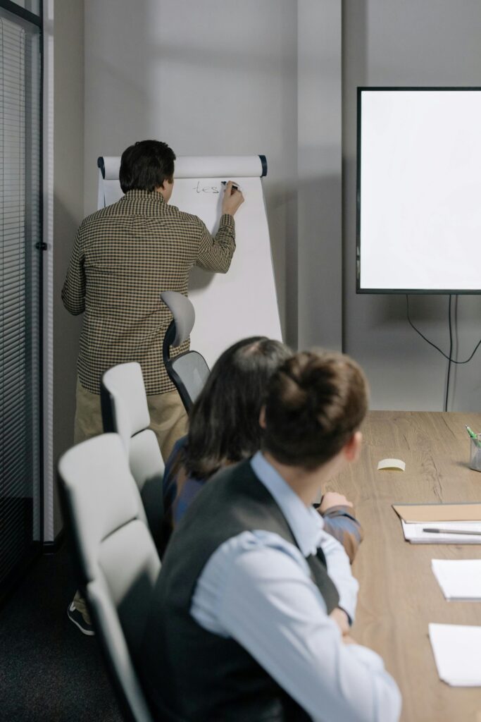 Services Three colleagues collaborating during an office meeting with a whiteboard discussion.